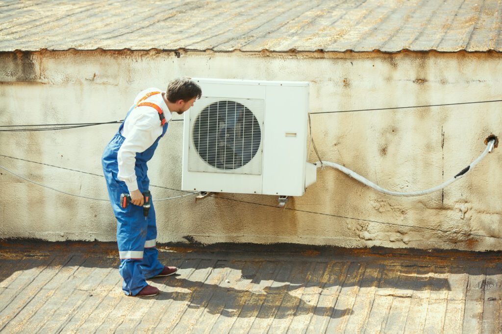 HVAC technician working on a capacitor part for condensing unit. Male worker or repairman in uniform repairing and adjusting conditioning system, diagnosting and looking for technical issues.